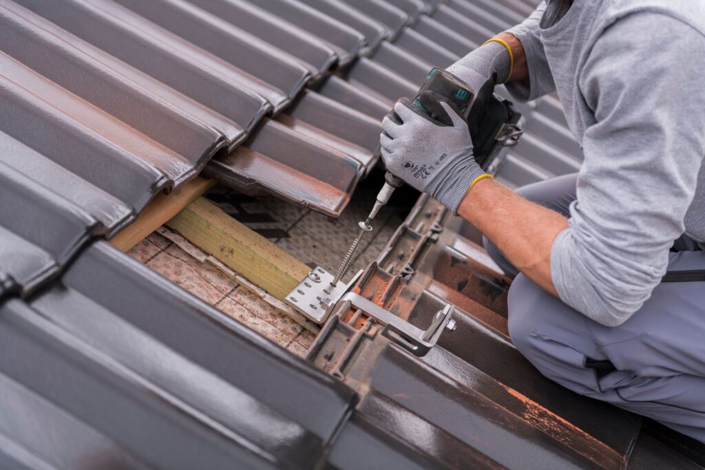 Handwerker befestigt eine Halterung für Solarmodule auf einem Ziegeldach, zeigt die Bedeutung der fachgerechten Installation und der Wahl eines kompetenten Photovoltaik Anbieters für eine sichere und effiziente Solaranlage.