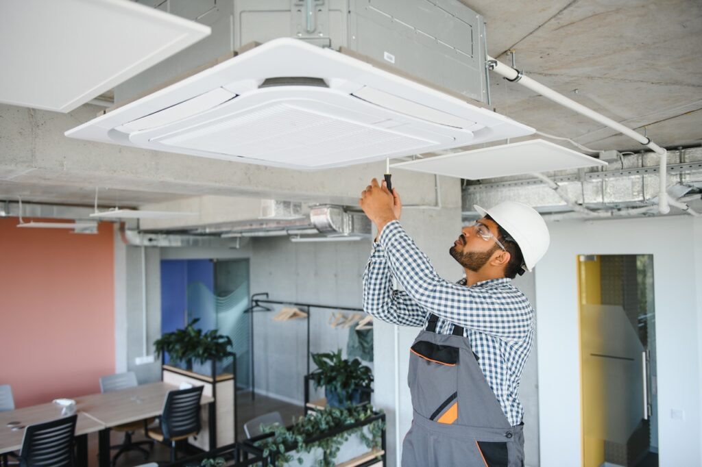 Techniker mit Schutzhelm und Werkzeug arbeitet an der Installation oder Wartung einer Klimaanlage in einem modernen Bürogebäude.