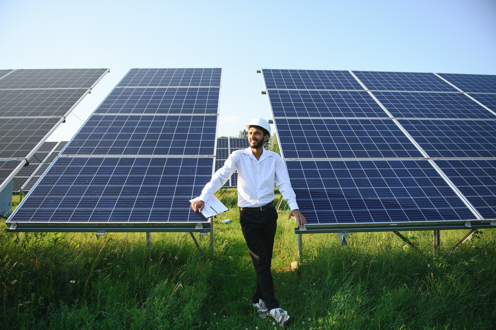 Mann mit Schutzhelm zwischen großen Solarpanels auf grüner Wiese | Nikotinsalz Liquid